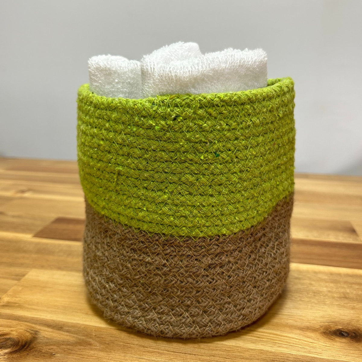 Green and brown woven basket with white towels on a wooden surface