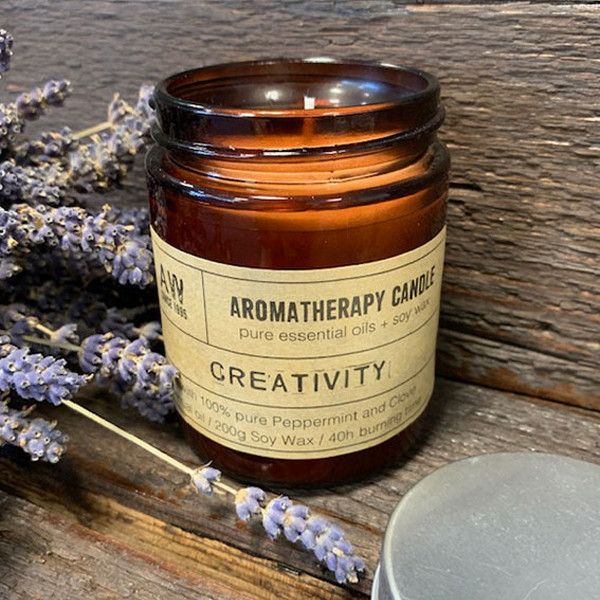 Aromatherapy candle labeled 'Creativity' with lavender on a wooden surface