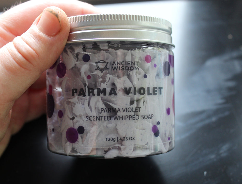Hand holding Whipped Soap Parma Violet jar with a black background