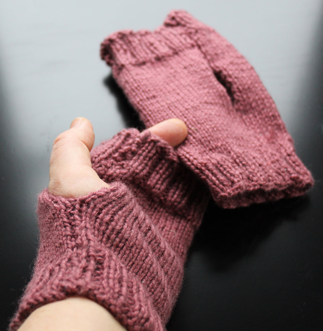 hand in plum coloured fingerless gloves on a black background