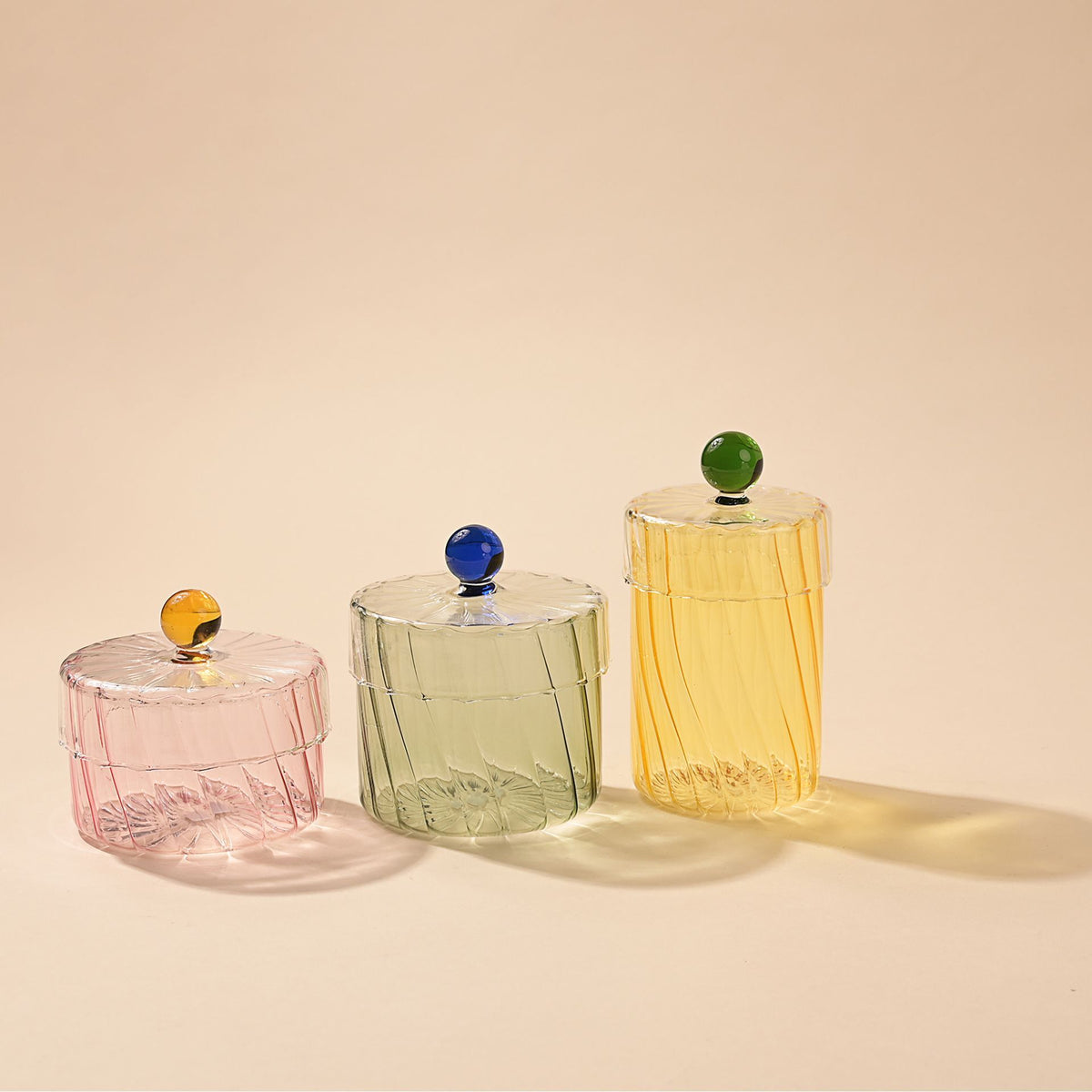 Three glass containers with colored lids on a beige background