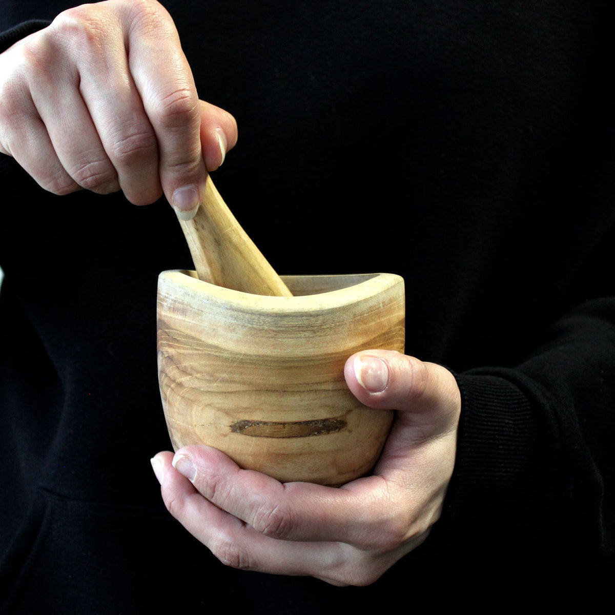 Wooden mortar and pestle being used against a black background