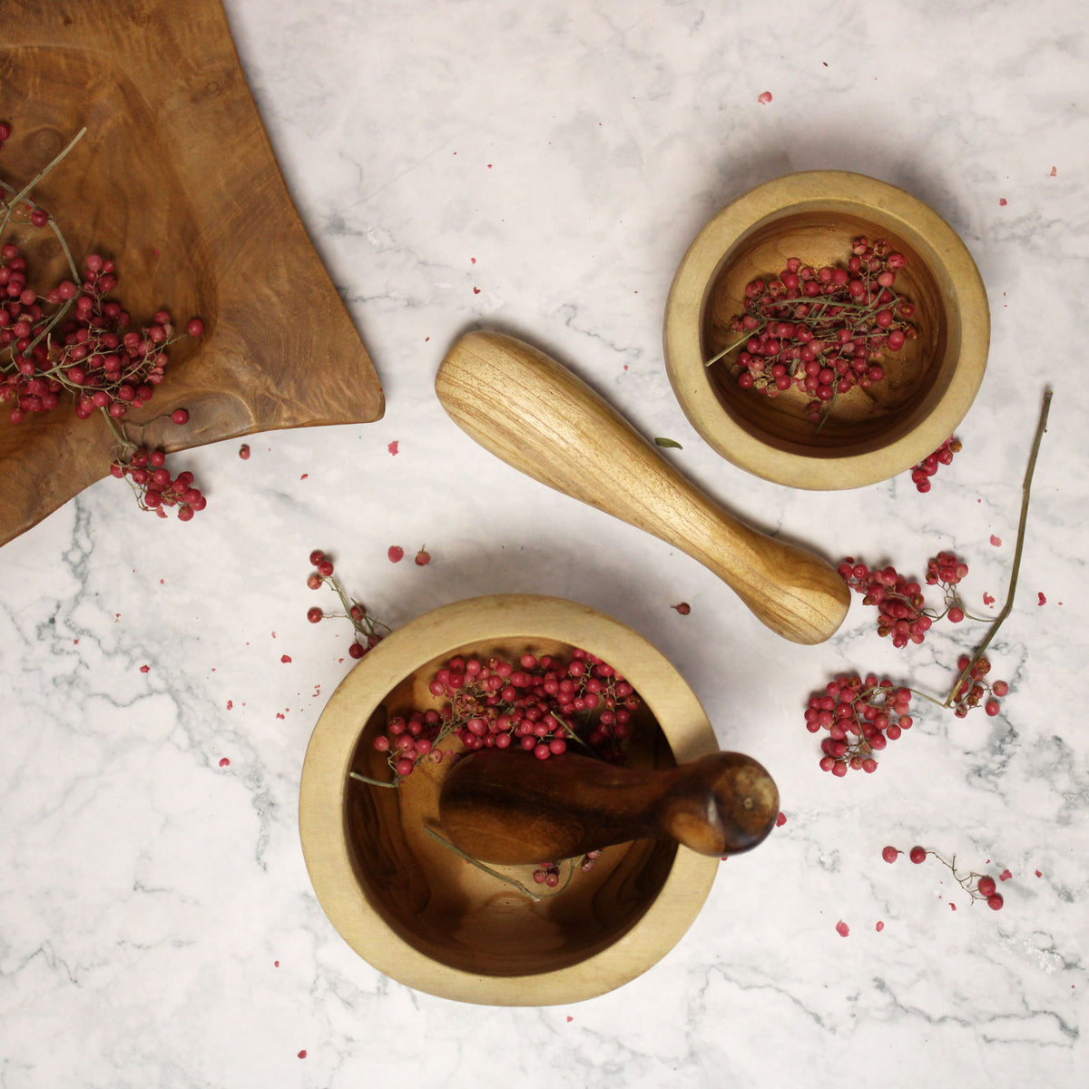 Wooden mortar and pestle with red berries on a marble surface