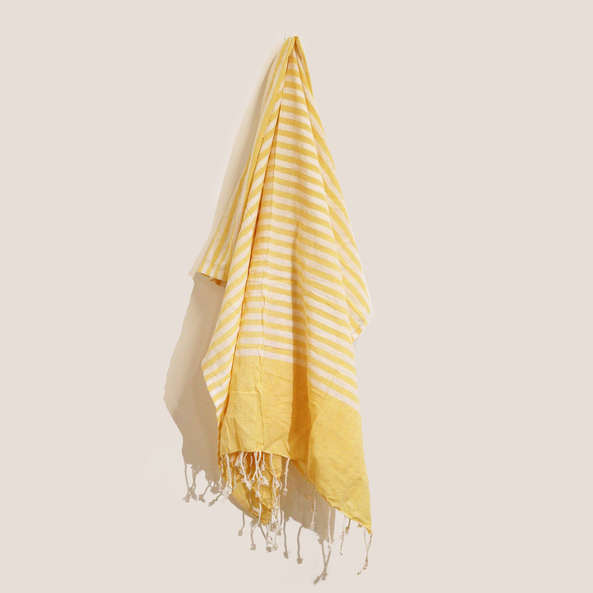 Yellow and white striped towel with fringes on a light beige background