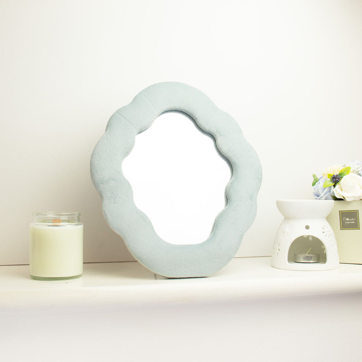 Decorative mirror with a textured frame on a white surface with a candle and small plant.