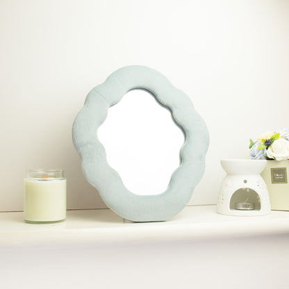 Decorative mirror with a textured frame on a white surface with a candle and small plant.
