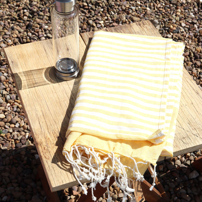 Yellow striped towel on a wooden surface with a glass bottle in the background.