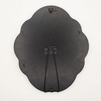 Black scalloped-edged back of a mirror showing hook and stand on a white background