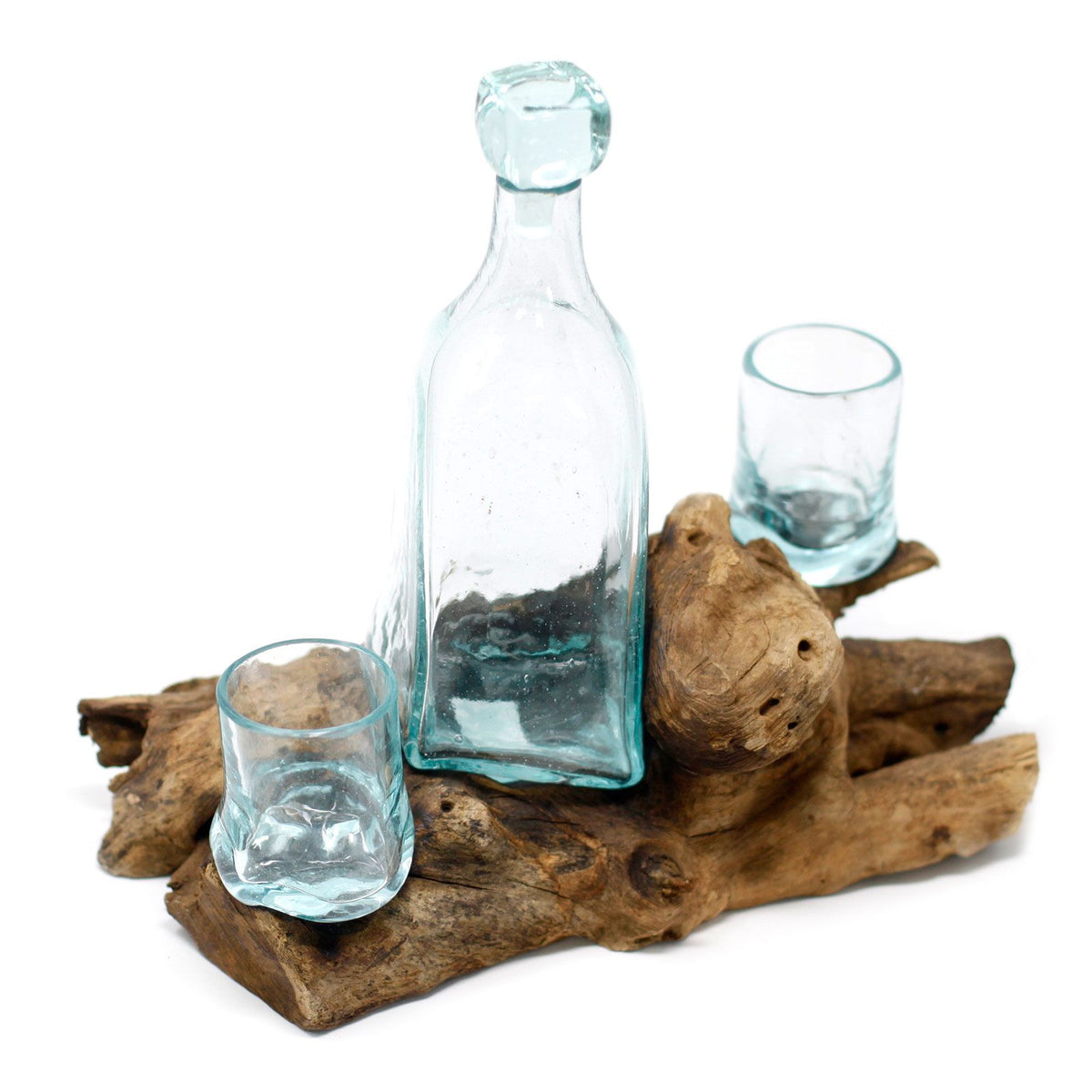 Clear glass bottle and two glasses on a piece of driftwood with a white background