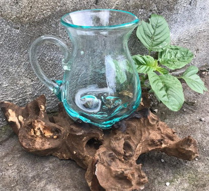 Turquoise glass pitcher on a piece of driftwood with green leaves in the background