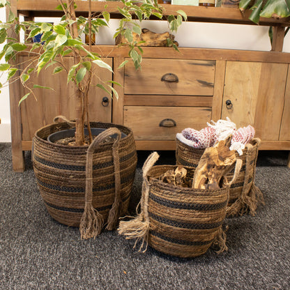 Set of three banana leaf seagrass baskets with plants on a carpeted floor.
