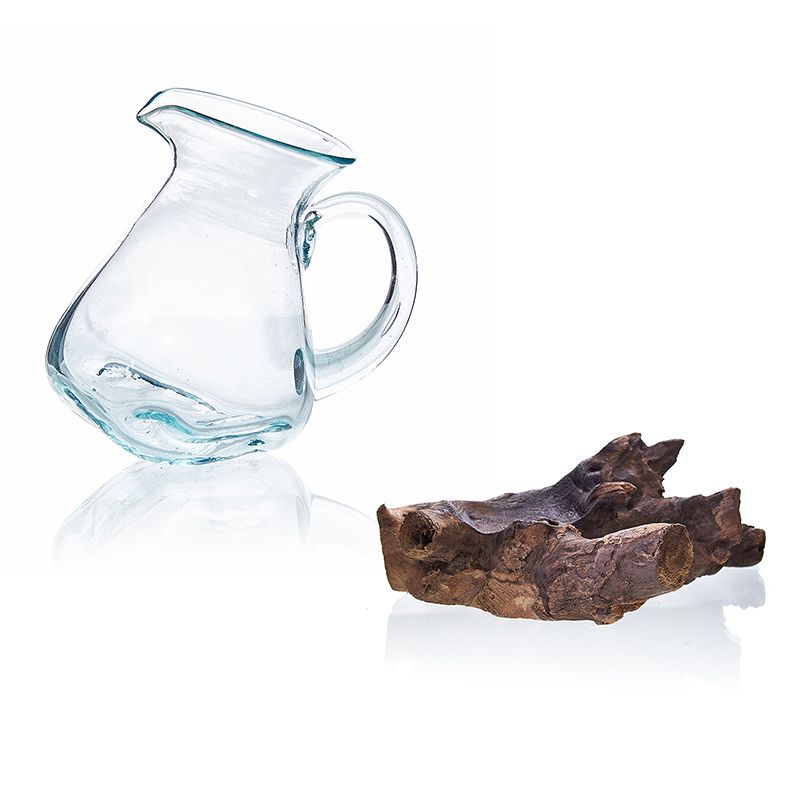 Clear glass pitcher next to a piece of driftwood on a white background