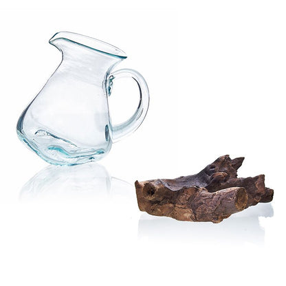 Clear glass pitcher next to a piece of driftwood on a white background