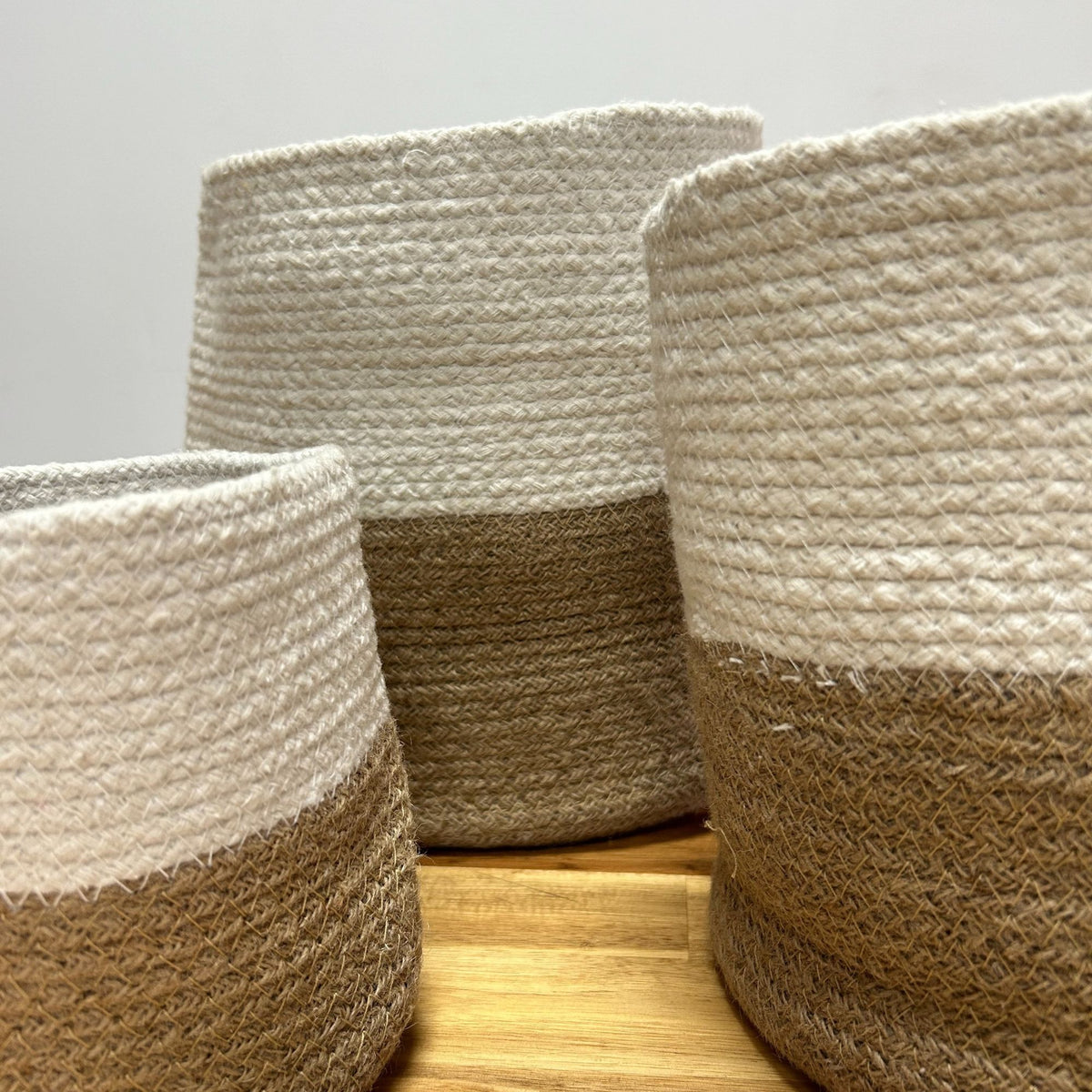 Three woven baskets with a two-tone design on a wooden surface.