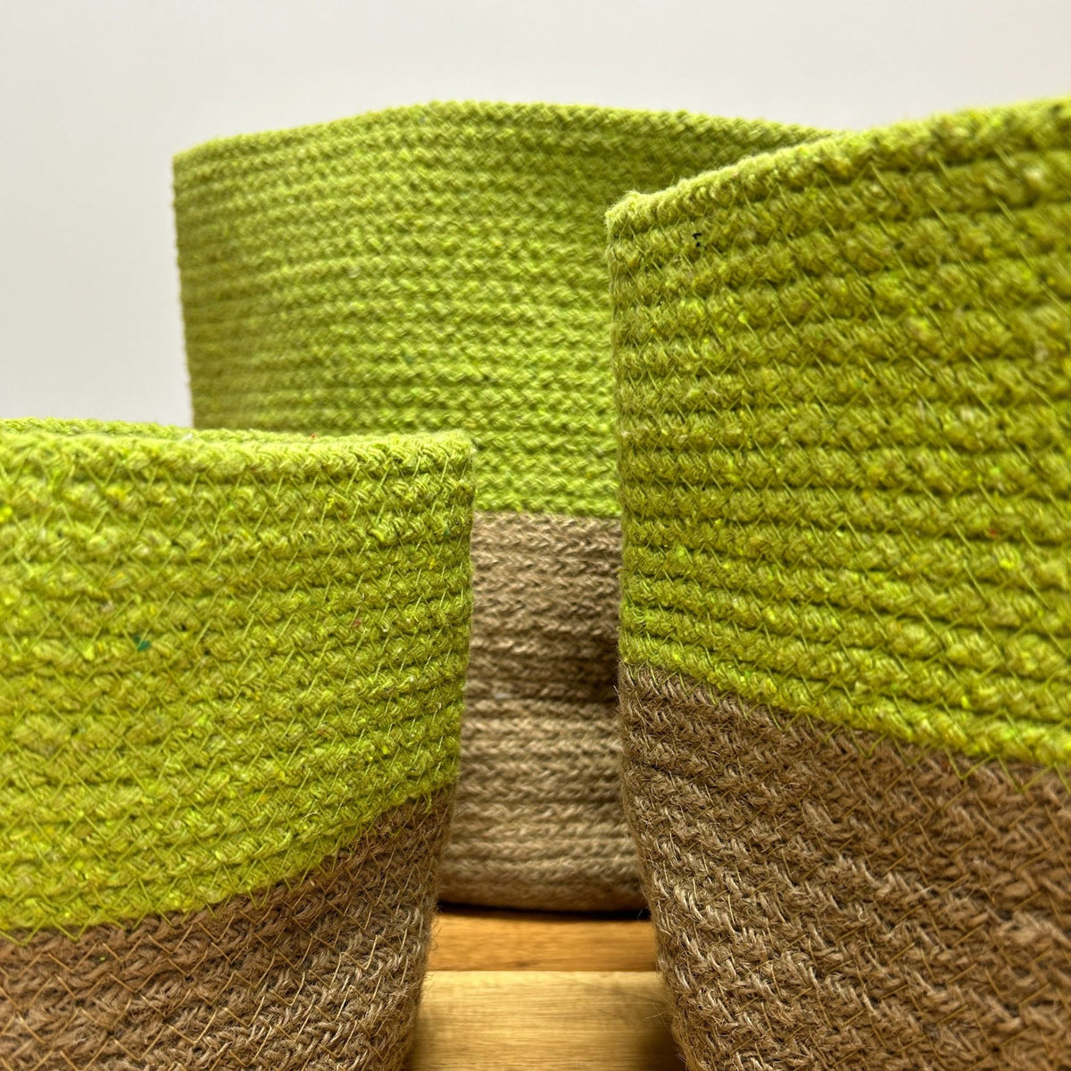 Three green and brown woven baskets on a wooden surface with a light grey background