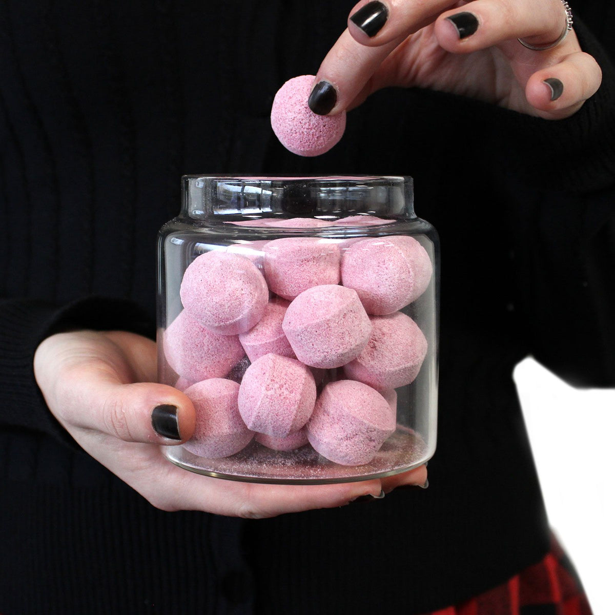 Person holding a glass jar filled with pink bath bombs against a black background