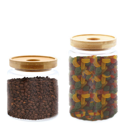 Two glass jars with wooden lids, one containing coffee beans and the other colorful gummy worms, on a white background.