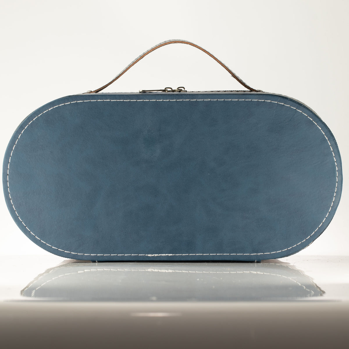 A blue oval leather clutch bag with a top handle, white contrast stitching, and a small metal clasp closure, shown on a reflective light gray surface against a white background.