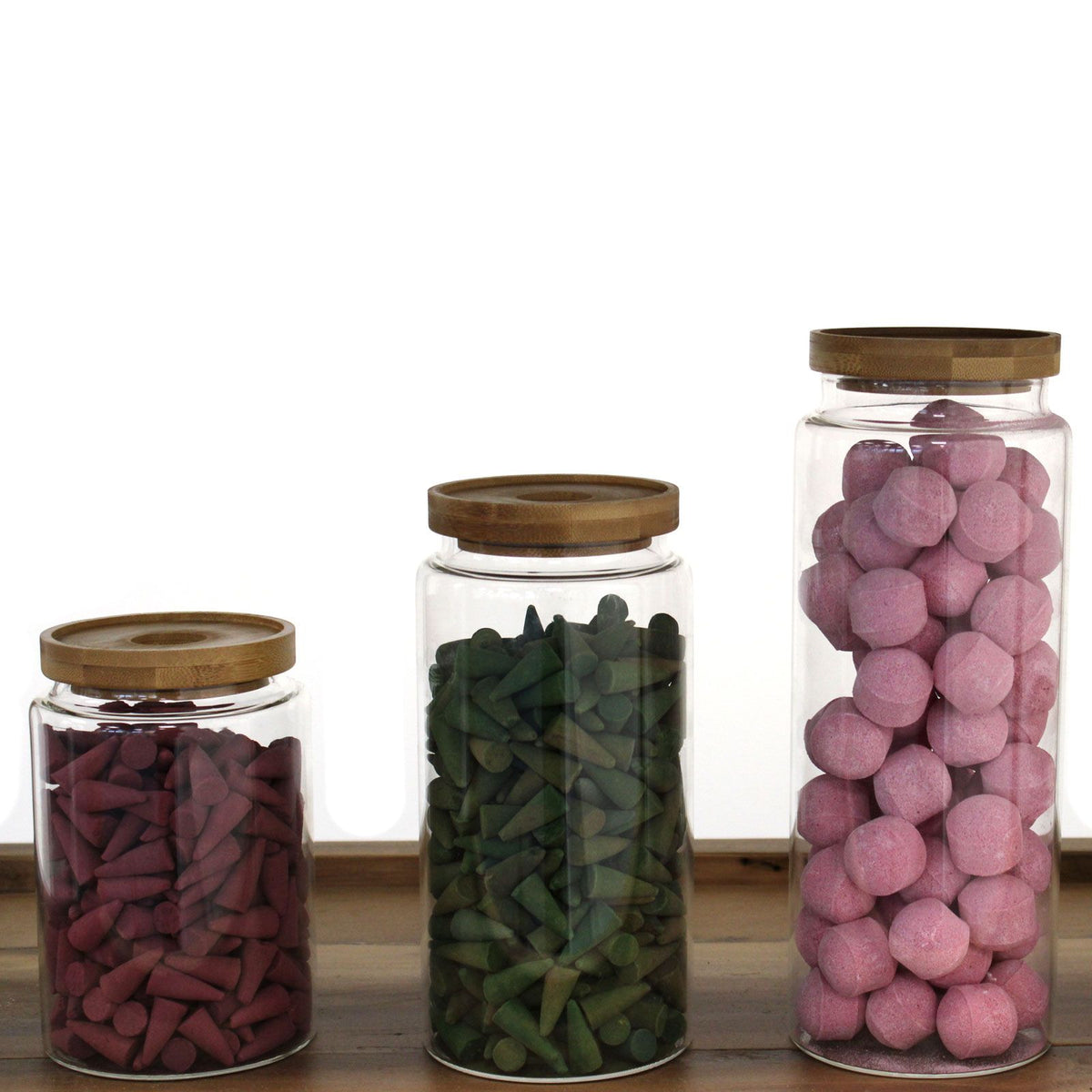 Three glass jars with wooden lids, each containing different colored items on a wooden surface.