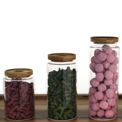 Three glass jars with wooden lids, each containing different colored items on a wooden surface.
