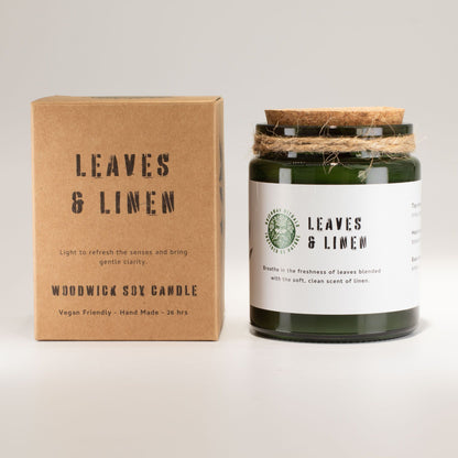 Woodwick candle labeled 'Leaves & Linen' with packaging on a light gray background