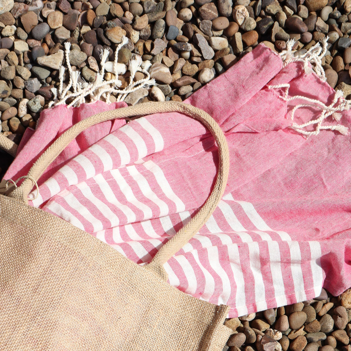 Pink and white striped towel with a beige bag on pebbles