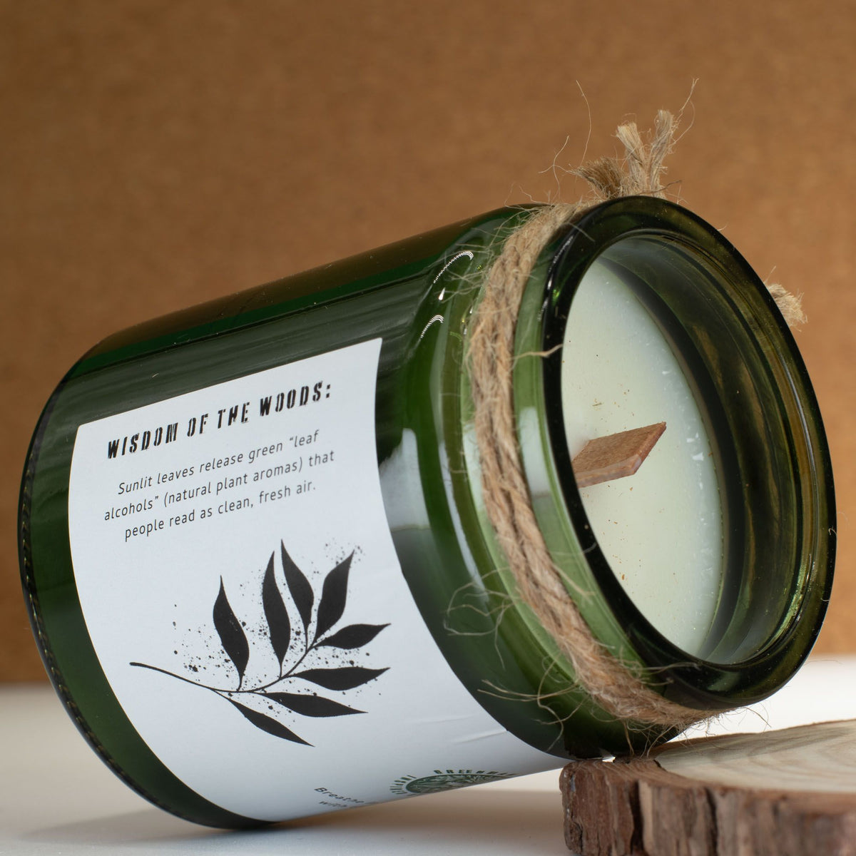 Green candle jar Woodwick Soy Candle Leaves Linen with a label on a wooden surface