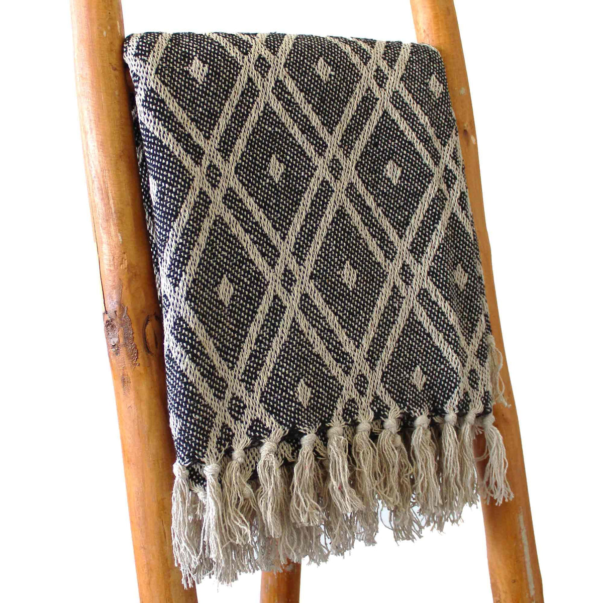 Black and white patterned throw blanket with tassels on a wooden ladder.