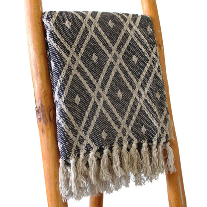 Black and white patterned throw blanket with tassels on a wooden ladder.