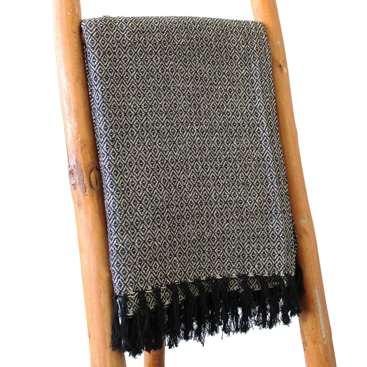 Black and white patterned throw blanket with fringes draped over a wooden ladder on a white background