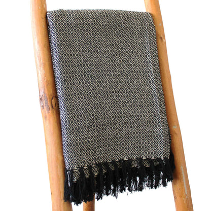 Black and white patterned throw blanket with fringes draped over a wooden ladder on a white background