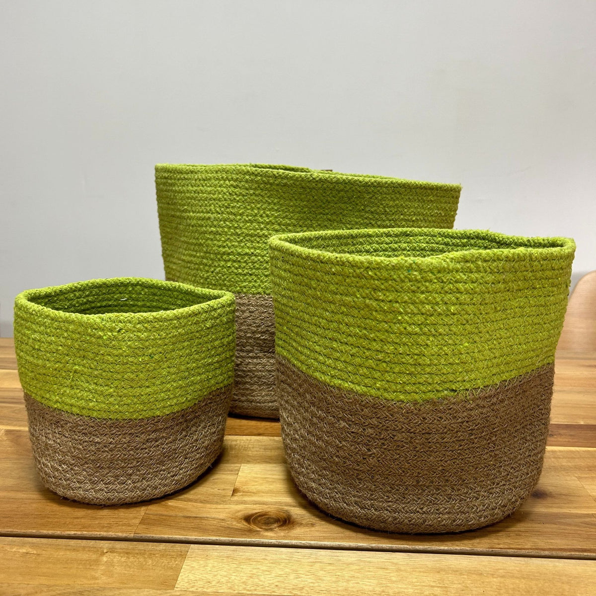 Three green and brown woven baskets on a wooden surface with a light gray background