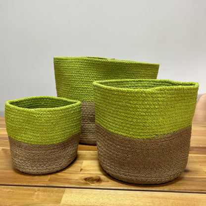 Three green and brown woven baskets on a wooden surface with a light gray background