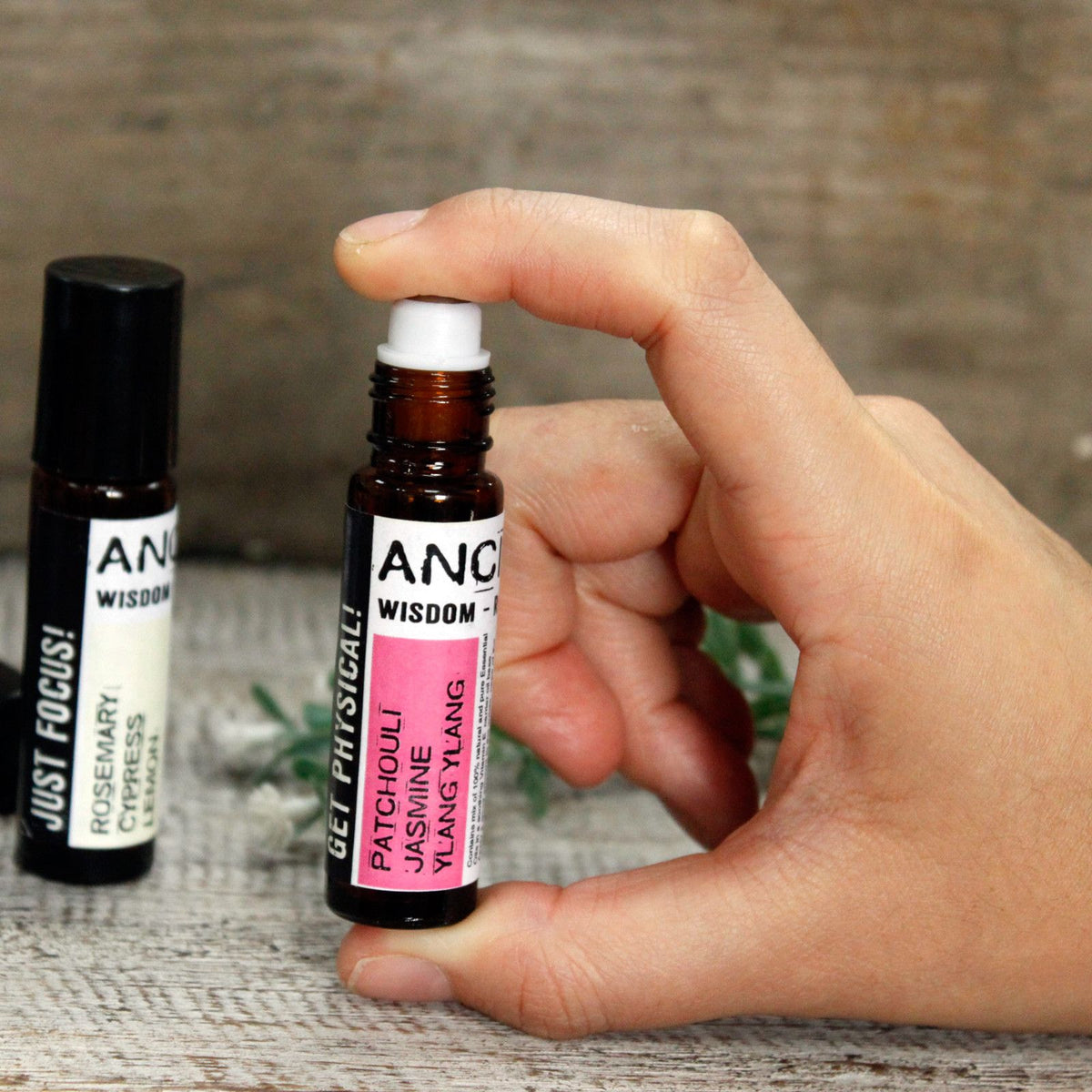 Hand holding a bottle of  Essential Oil Roll on  with another bottle in the background.