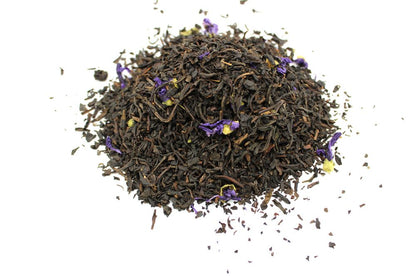 Dry black tea leaves with purple flowers on a white background