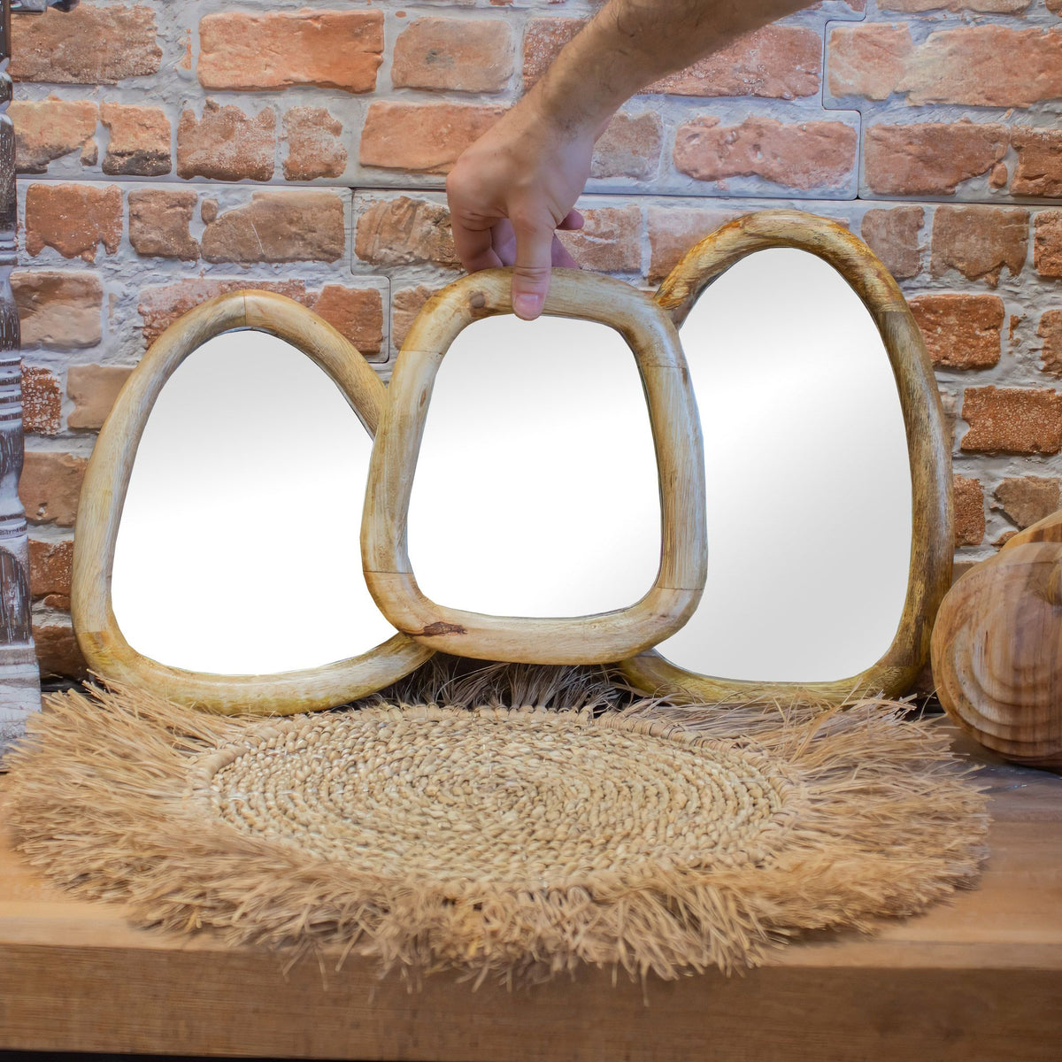 Pebble shaped mirrors set of 3 with wooden frames on a textured surface against a brick wall.