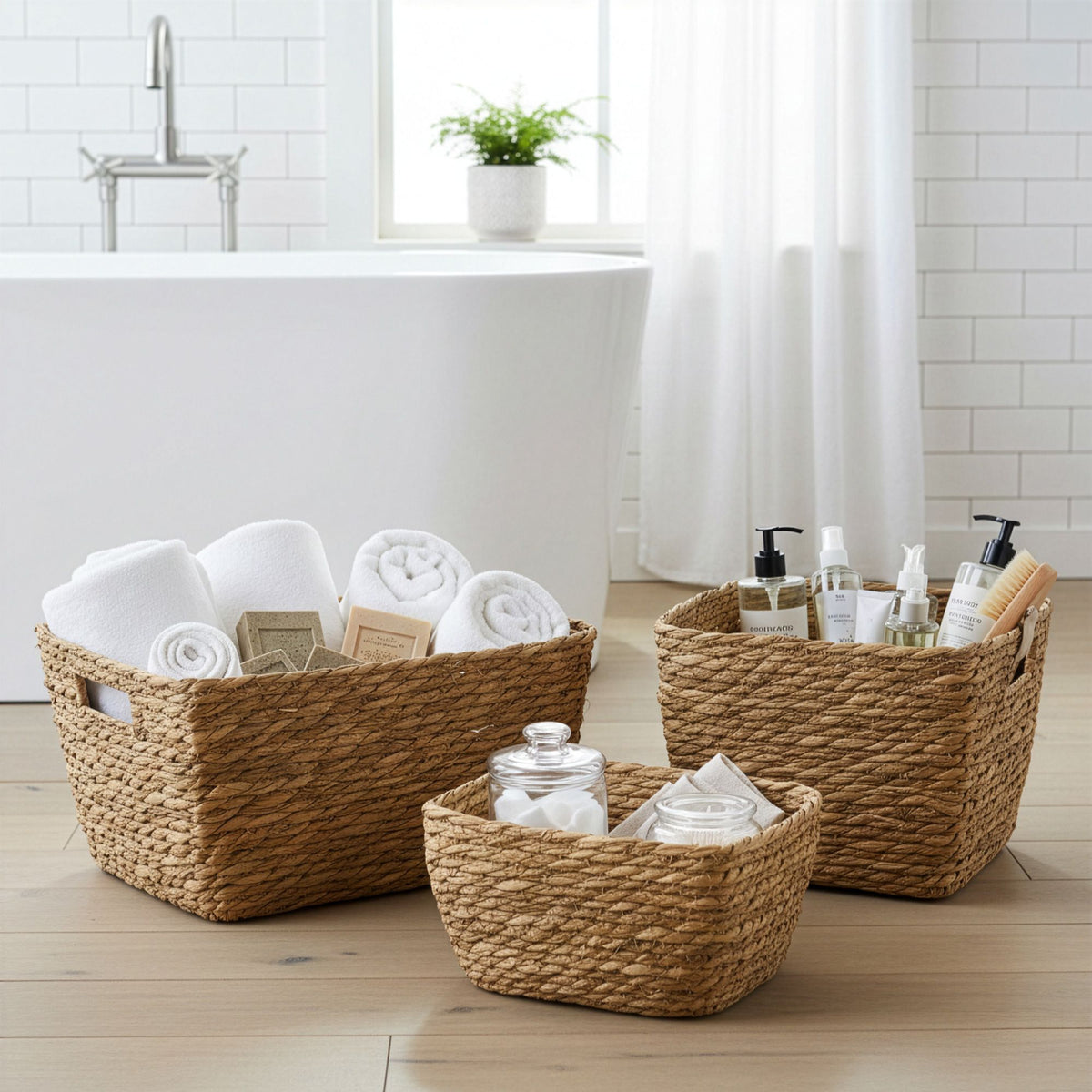 Three seagrass square baskets containing towels and toiletries in a bathroom setting.