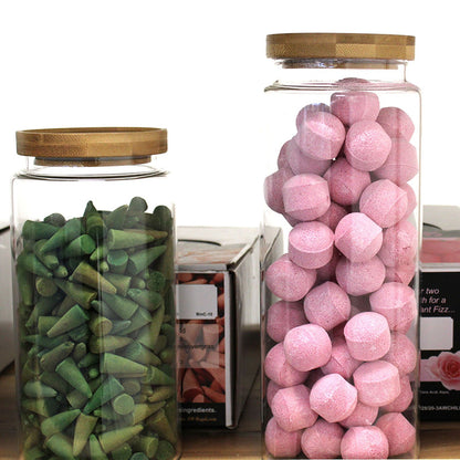 Two glass jars with wooden lids, one containing green candy and the other pink candy, on a white background.
