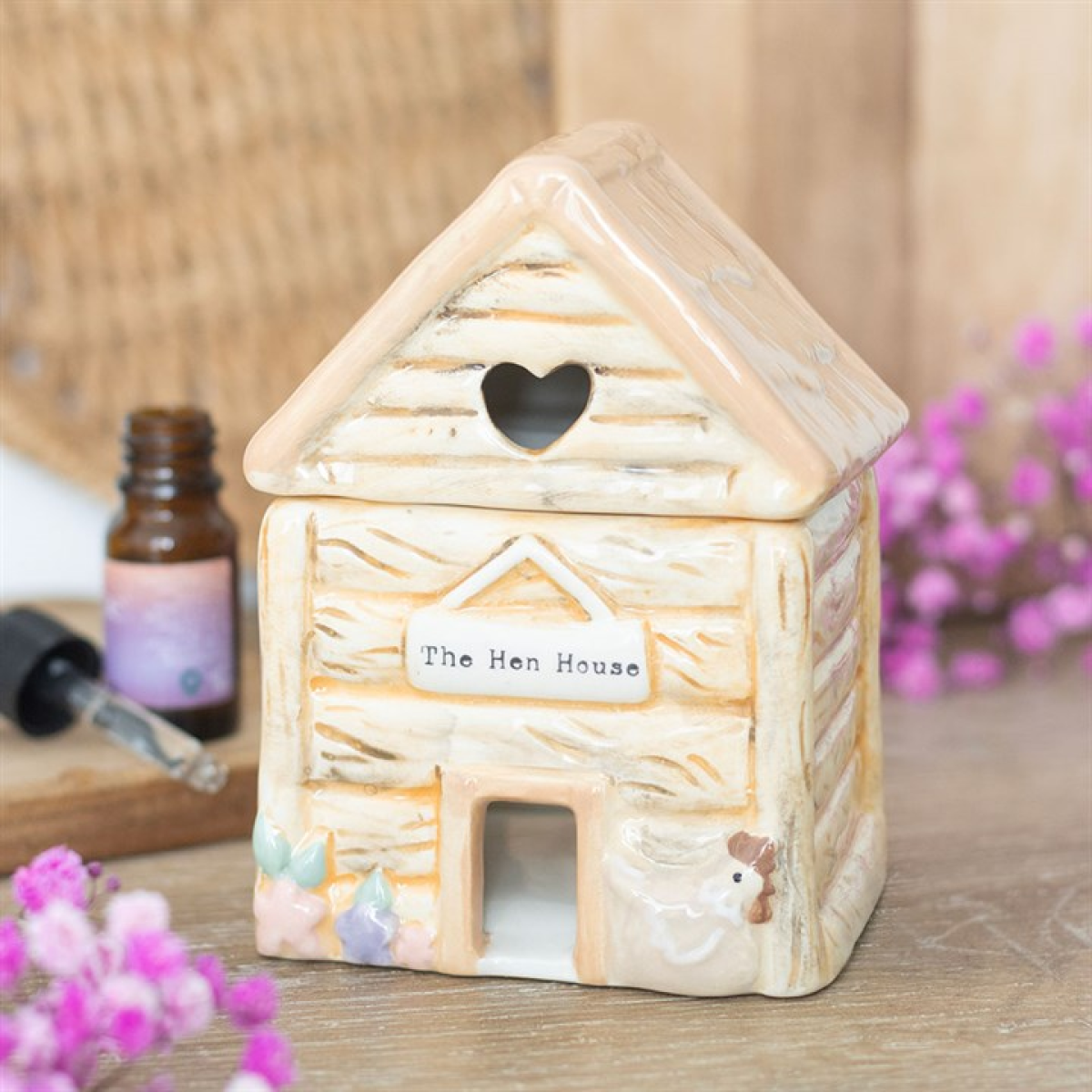 Decorative Ceramic Hen House Oil Burner with 'The Hen House' label on a wooden surface with flowers and a bottle.